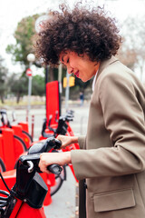 young latin woman taking a bike from a rental station, active lifestyle and sustainable mobility concept