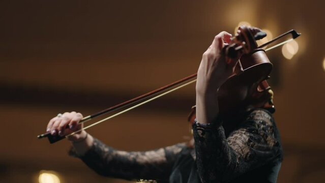 female musician is playing fiddle in music hall, portrait of woman with violin, concert in opera house