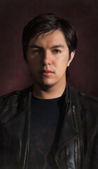 portrait of young man looking to camera with long hair and leather jacket with red background 
