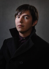 young mexican man whit white skin fine art portrait with gray background , long hair and brown eyes and black coat 