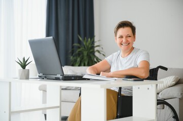 Freelancer in wheelchair using laptop near notebook and papers on table