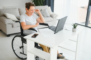 Middle age woman using laptop sitting on wheelchair at home