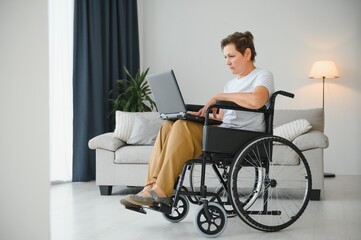 Middle age woman using laptop sitting on wheelchair at home