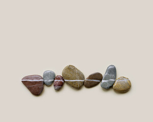 Aesthetic minimal flat lay sea pebble stones with white line, beige background. Composition from natural colored stone on the same level. Balance or harmony concept, horizontal row rocks.