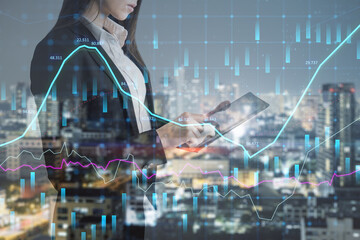 Fototapeta na wymiar Attractive young european businesswoman with tablet standing on abstract night city background with glowing forex chart. FInance, trade and money concept. Double exposure.