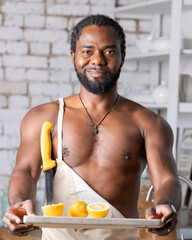 Black man cooking breakfast or lunch on kitchen at home. African American man wearing an apron preparing lemon.