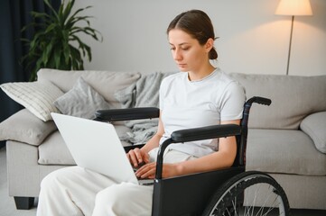 Female freelance programmer sitting in wheelchair and using computers while coding web game at home.