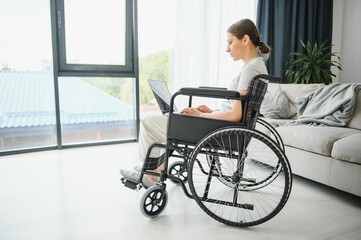 Freelancer in wheelchair using laptop near notebook and papers on table