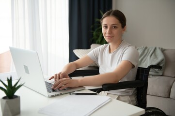 woman in a wheelchair works on the laptop PC in the home office with an assistance dog as a...