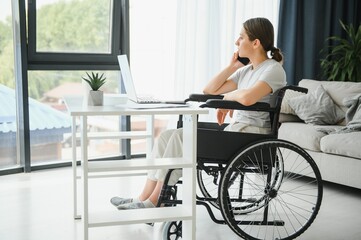 Female freelance programmer sitting in wheelchair and using computers while coding web game at home.