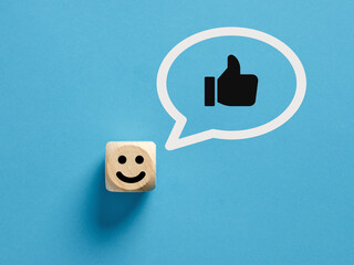Happy face icon on a wooden cube with like or thumb up gesture in a speech bubble.