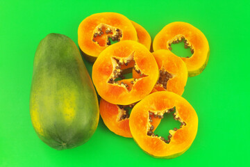 Papaya fruit slices and whole papaya fruit on green background.