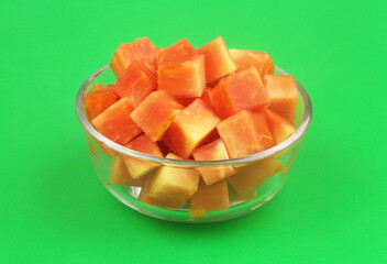 Sliced red papaya fruit in bowl on green background	