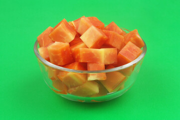 Glass bowl with sliced papaya fruit on green background