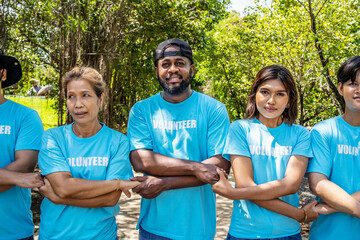 Portrait of smiling male and female volunteers standing with arms around. Multiracial group of confident activists are in park. They are volunteering for environmental cleanup.