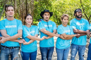 Portrait of smiling male and female volunteers standing with arms around. Multiracial group of confident activists are in park. They are volunteering for environmental cleanup.