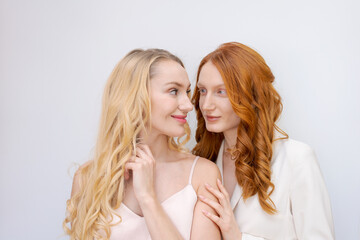 Obraz na płótnie Canvas Close-up fashion portrait couple of two pretty women, best friends smiling on light background. Variable wavy hairstyle. Blonde and redhead posing