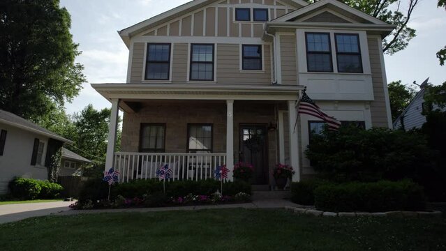 Boom up front of house with American flag waving and patriotic decorations in front to reveal a sunny sky above.