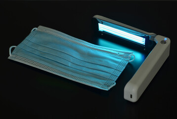 Portable quartz lamp with blue light disinfect medical mask on dark background from bacteria,...
