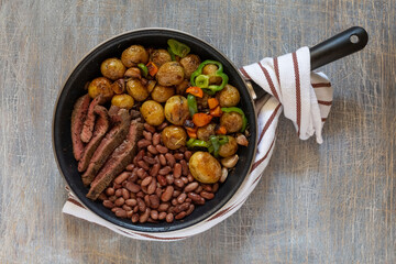 Large fried piece of ham meat in a pan with vegetables and spices, American lunch fried piece of meat and potatoes, beans in sauce and snacks, copy space for text