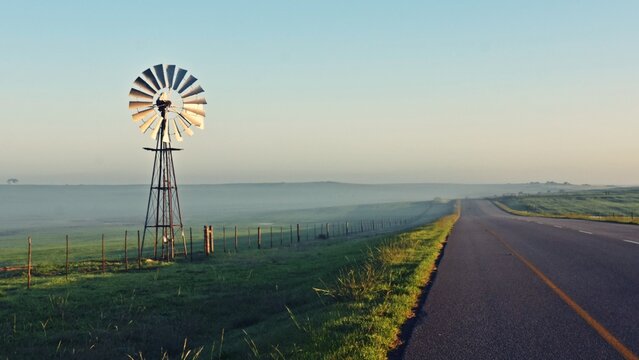 Landscape with a Windmill water pump and a county road with morning fog