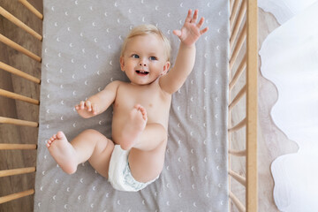 Upper view of little playful baby boy in diaper lying on his back reaching hand out to touch toy or...