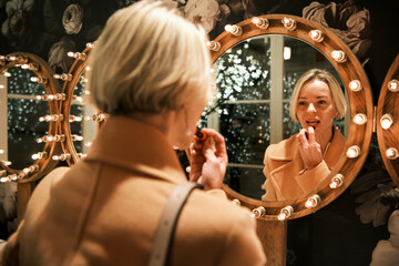 Beautiful woman applying lipstick looking in mirror
