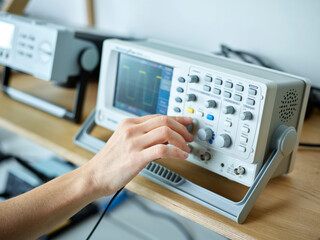Hand of engineer adjusting oscilloscope in electronic laboratory