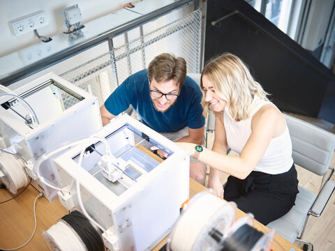 Smiling engineers discussing over 3d printer at workshop