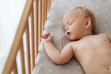 Closeup portrait of cute blond little boy with soft skin sleeping in his bed during nap time in his...