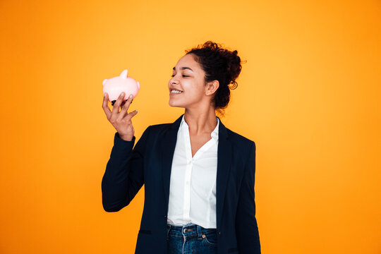 Smiling businesswoman with piggy bank standing against yellow background
