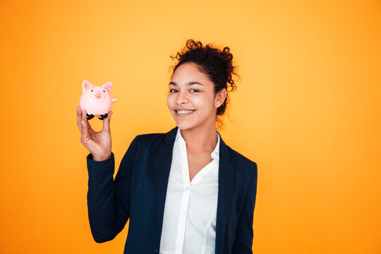 Happy businesswoman with piggy bank standing against yellow background