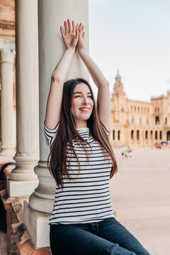 Smiling ballet dancer with arms raised leaning on column at Plaza de Espana in Spain
