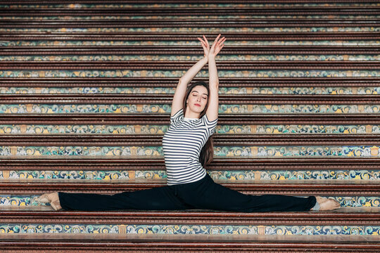Ballet dancer with arms raised practicing splits on staircase at Plaza de Espana