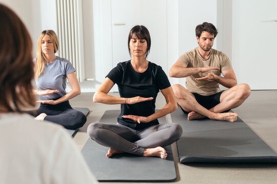 Man and women sitting on exercise mats practicing relaxation exercise in yoga studio