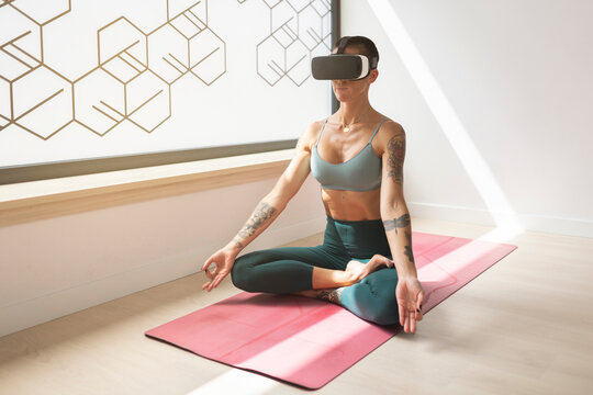Woman practicing lotus position on mat wearing virtual reality headset in studio