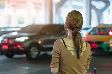 Back view of Asian female passenger with big roller luggage stand to wait for the car to pick up at...