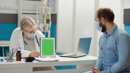 Obraz premium Senior medic and patient using greenscreen on digital tablet during covid 19 pandemic. Doctor showing blank mockup background with isolated copyspace chromakey on template to patient. Tripod shot.