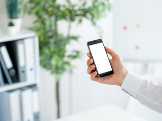 Virtual connection. Digital mockup. Office place. Unrecognizable man holding smartphone with blank screen in light room interior.