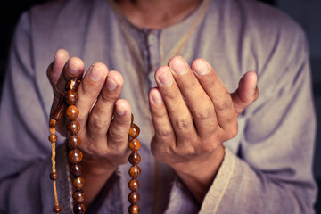 Muslim man in brown session lift two hand for praying and wearing bead on hand to determine the number of prayer services.concept for Ramadan, Eid al Fitr, eid ad-ha, meditation, islamic praying