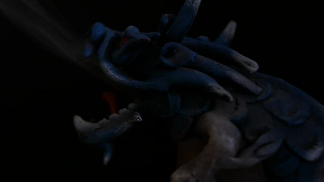 close up shot of an dragon statue exhaling fumes while the light source fades away