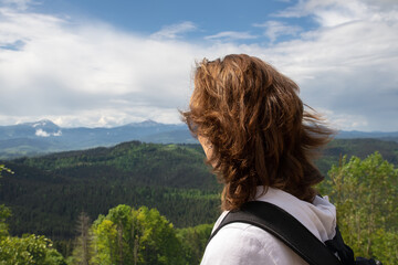 Portrait young adult woman enjoy adventure trekking looking over awesome mountain forest panoramic view with blue sky background. Female hiker watch tranquil horizon alpine landscape panorama