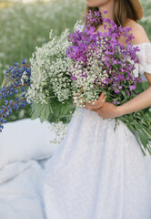 Young woman holding bunch of beautiful field flowers while staying in the field. Close up. Creative photoshoot. Art.
