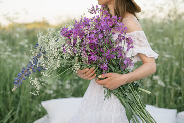 Young woman holding bunch of beautiful field flowers while staying in the field. Close up. Creative photoshoot. Aesthetics.