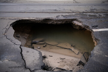 Huge sinkhole on busy asphalt road surface on which cars drive. Accident situation on a city street...