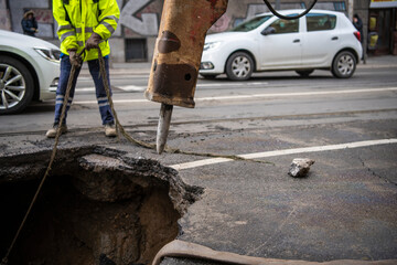 Road construction worker with machines repair Huge sinkhole on busy asphalt road surface on which...