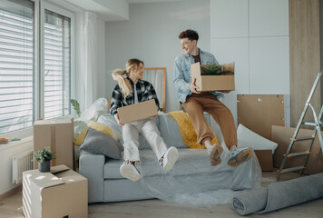 Cheerful young couple in their new apartment, carrying boxes. Conception of moving.