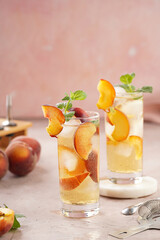 Two glasses with refreshing cocktail with ice cubes, peach slices and fresh mint on pale purple background