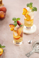 Two glasses with refreshing cocktail with ice cubes, peach slices and fresh mint on pale purple background
