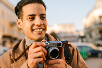 Obraz premium Young man wearing coat taking photo on retro camera in autumn park